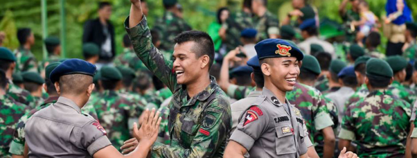 Personel TNI dan Polri berseragam saling berinteraksi dengan semangat kebersamaan di ruang terbuka hijau.