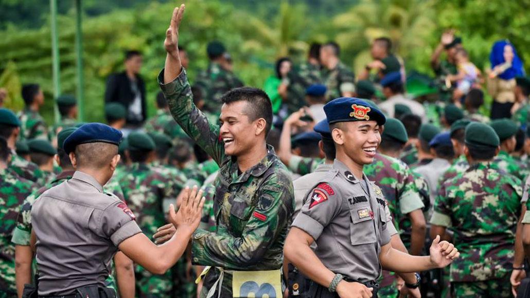 Personel TNI dan Polri berseragam saling berinteraksi dengan semangat kebersamaan di ruang terbuka hijau.